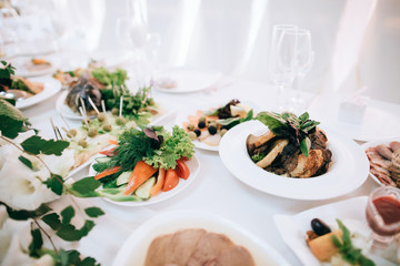 Wedding reception white table arrangement, floral centerpiece decoration, food. Catering service.