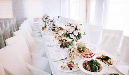 Wedding reception white table arrangement, floral centerpiece decoration, food. Catering service.