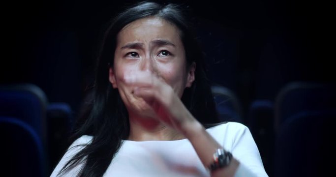 A asian woman wipes away her tears while watching an emotional movie.