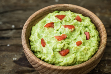 Guacamole with Pieces of Tomato in a Bowl on Rustic Wooden Table