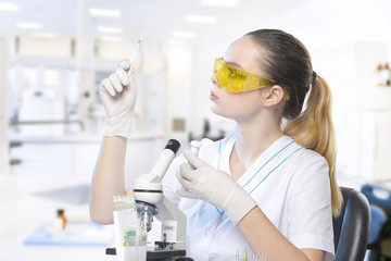 Closeup of a beautiful lab assistant girl in glasses with a microscope on a desk on a laboratory background.