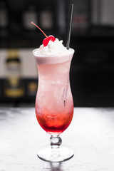 Strawberry soda topped with whipped cream and cherry in tall glass, dark background