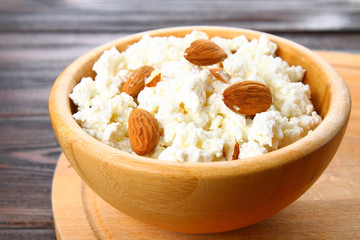 Homemade cottage cheese with almonds and raisins in a bowl on a wooden table.