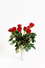 Obraz premium Close up, low angle view shot of spray or bouquet of red roses as gift for Valentine's Day and romantic symbol for love in light grey vase on white background
