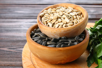Black peeled and unpeeled sunflower seeds in a wooden bowl on a wooden table.