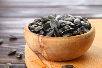 Black unrefined sunflower seeds in a wooden bowl on a wooden table.