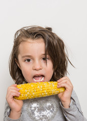 Indoor close-up portrait of young girl  eating corn-cob isolated on a white background.