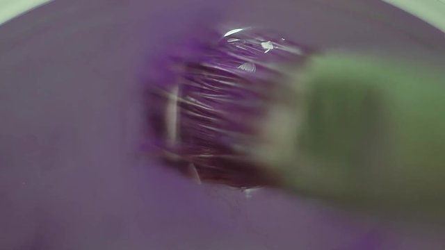 Paintbrush with purple color paint bathe into water glass, macro close up
