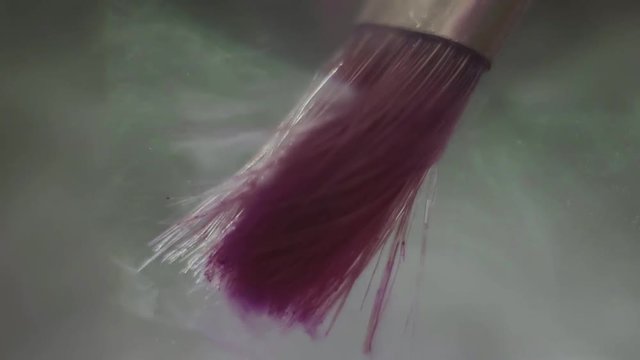 Beautiful purple color paint shape floating of brush in fluid against glass black background, macro close up