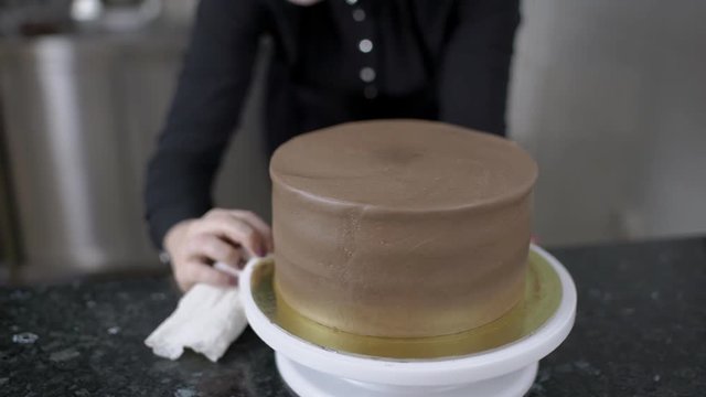 Female confectioner is cleaning the plate with chocolate cake for birthday party. Dish is white, with dolden decore and woman is using napkin in her hand with beautiful manicure to delete sweet paste