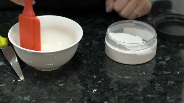 In a glass bowl woman paddles the white mixture with a spatula. Close-up on table person mixes white powder with water using a silicone tool. slow motion slowmotion