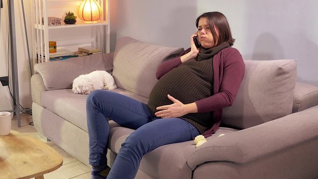 Pregnant woman having contractions at home on sofa calling for help medium shot