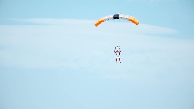Parachuting activity, skydiving rig. Jumper dressed in parachute equipment landing on the ground. Flying in a sunny summer day. Slow motion video
