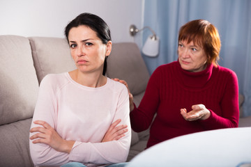 Sad mature female and daughter at sofa after quarrel