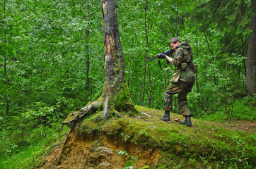 Fototapeta premium soldier aims and shoots standing in a fighting stand on a hill in the forest