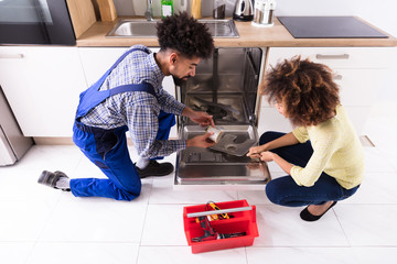Repairman Fixing Dishwasher In Kitchen