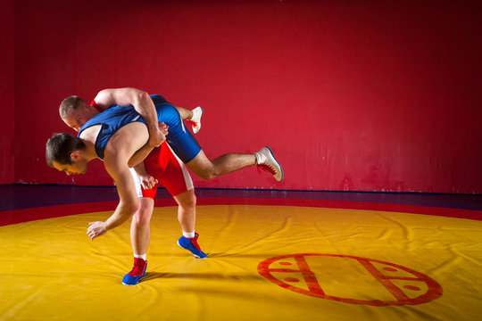 Two greco-roman  wrestlers in red and blue uniform wrestling  on background on a yellow wrestling carpet in the gym