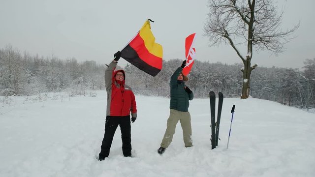 National flag of Switzerland and Germany waving in the wind with blurred mountains in the background. Two people hold the flags in a blizzard and a strong wind