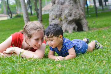 Naklejka na ściany i meble Happy biracial family in the summer park - caucasian mother with her latin son laying on the grass.