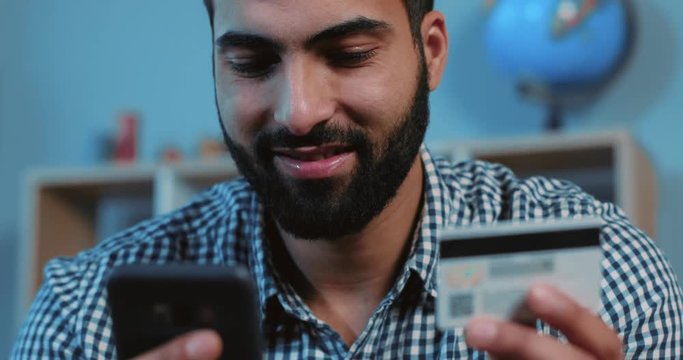 Close up face young happy man buying online uses a phone and a credit card on sofa home shopping cellphone device hand holding lifestyle smart business internet technology bank banking cash