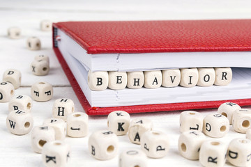 Word Behavior written in wooden blocks in notebook on white wooden table.