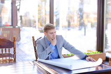 Student of architecture faculty sitting at cafe table and looking at drafting work. Young male...