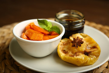 On the plate is a baked pumpkin, an apple and a glass jar with honey, near anise, mint. Wicker substrate and wooden table, composition. Close-up