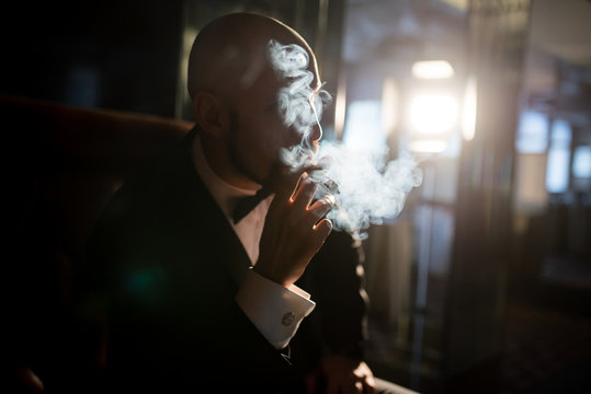 A brutal man in a dress coat smokes a cigar.