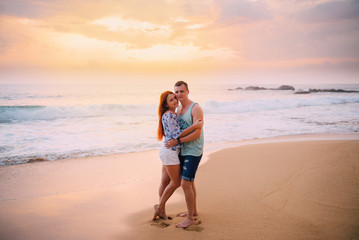 pair of young lovers stand on the beach near the ocean and look at the camera