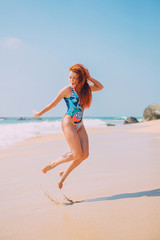 happy young red-haired woman jumping on a tropical beach on a sunny afternoon