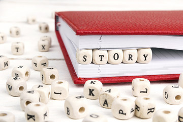 Word Story written in wooden blocks in red notebook on white wooden table.