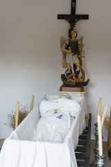 A figurine of a mortal in an open coffin in a village morgue.