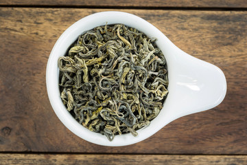 dry tea leaves in a white cup on wood,top view