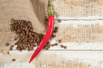 coffee beans in a bag scattered on a wooden background with a sharp red pepper background