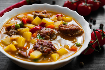 Bowl of sausage soup with mix vegetables on a dark wooden background