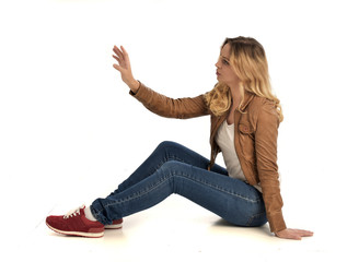 full length portrait of girl earring leather jacket and jeans, seated pose  on white studio...