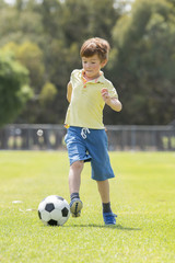 little kid 7 or 8 years old enjoying happy playing football soccer at grass city park field running and kicking the ball excited in childhood sport passion