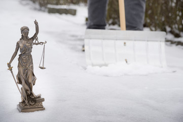 Ab wann muss man Schnee räumen? - Justitia Statue im Vordergrund, im Hintergrund fegt ein Mann den...