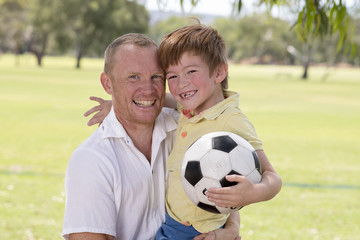 young happy father carrying on his back excited 7 or 8 years old son playing together soccer football on city park garden posing sweet and loving