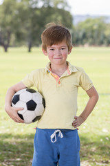 young little kid 7 or 8 years old enjoying happy playing football soccer at grass city park field posing smiling proud standing holding the ball