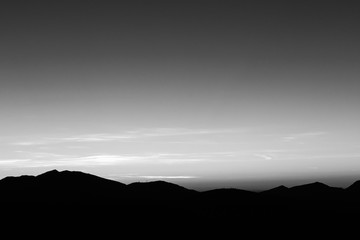 A silhouette of a mountain peak at sunset, under a big , almost empty sky