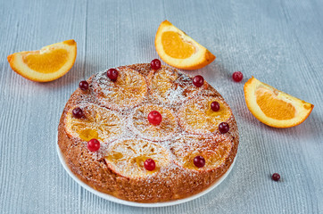 Citrus pie with caramelized oranges and powdered fresh red berries on the gray surface. Just backed pie with raw orange slices and cranberries on the gray background. Side view