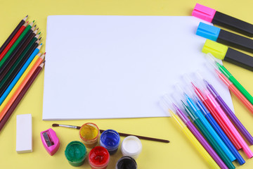 paper with colored crayons, brush, pencils and paints on yellow background. Top view . Flat lay image.Working desk table concept.