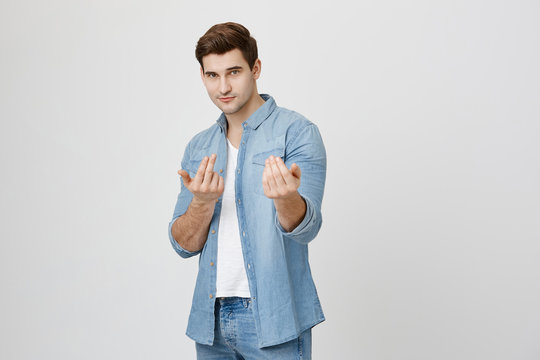 Portrait Of Attractive Confident Guy With Stylish Haircut, Wearing Denim Clothes, Showing Come To Me Gesture While Looking At Camera And Standing Over Gray Background. You Want Fight, You Will Get It