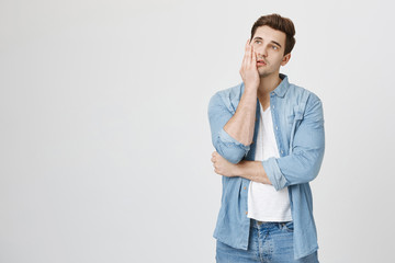 Tired and annoyed handsome boy holding palm on cheek and looking up, expressing boredom while...