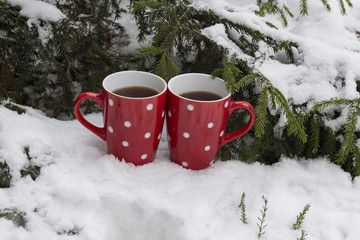 on the snow under the Christmas tree two red mugs with tea. Celebration, Valentine, Christmas, new year background.
