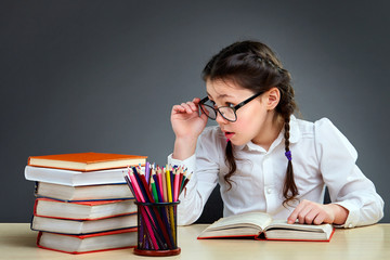 Cheerful enthusiastic cute little girl in glasses reading books and pointing her finger on the grey...