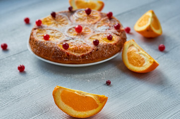 Fototapeta na wymiar Juicy orange slice on the foreground close up. Homemade orange cake with fresh red cranberries and oranges on the blurred background. Citrus cake on the gray table