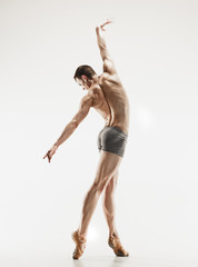 Athletic ballet dancer in a perfect shape performing over the grey background.