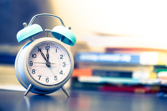 Wecker auf Schreibtisch, B&uuml;cher im Hintergrund